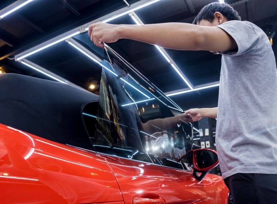 Applying tinting foil on a car window in a auto service. Red car at background